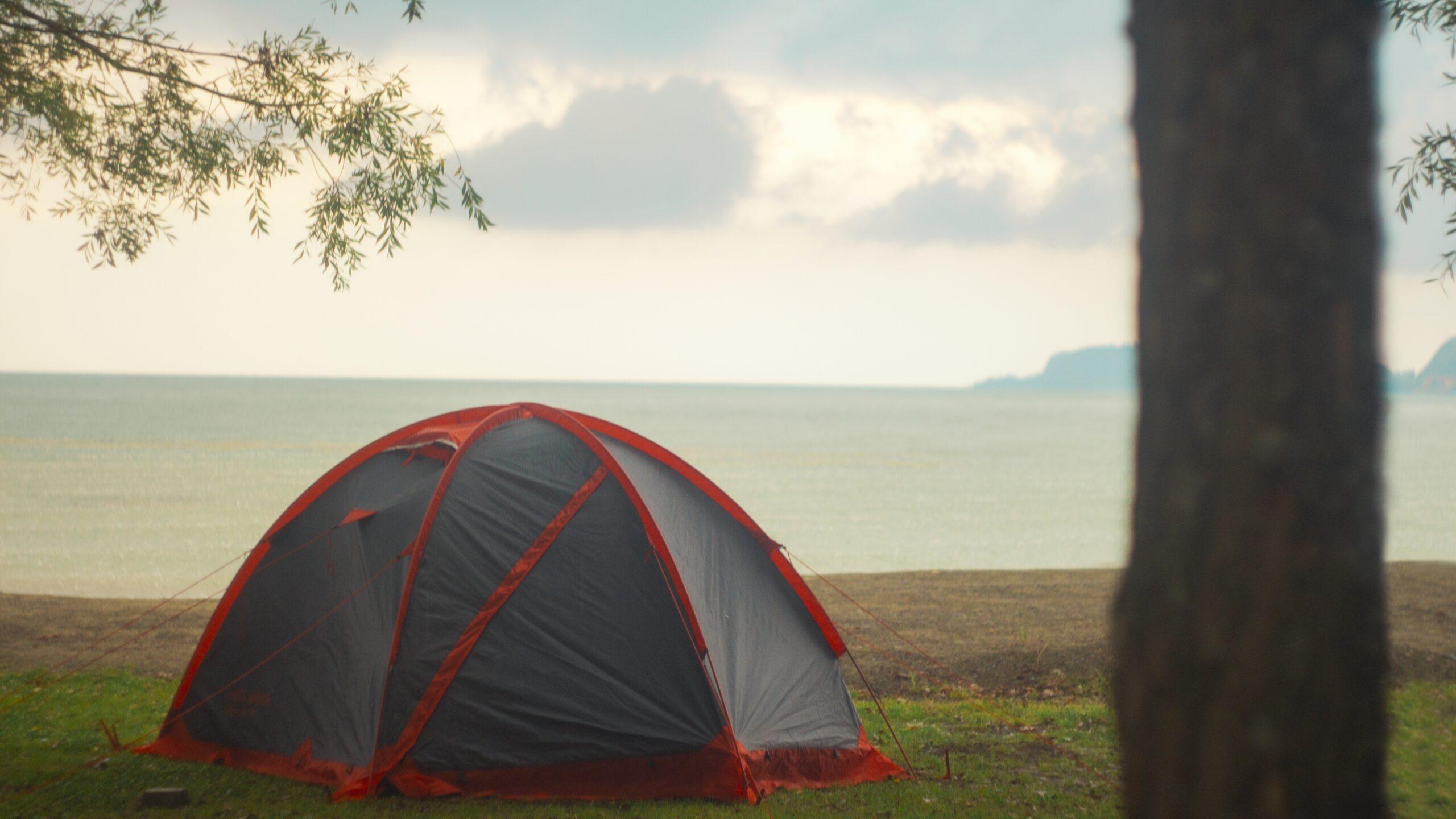 A black and red tent on the shore near the beautiful sea under the cloudy sky